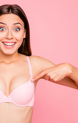 smiling young woman pointing to her breasts, wearing a pink bodice, pink background