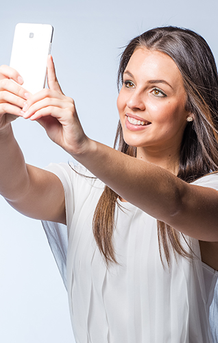 Young woman smiling, while taking a selfie with her cell phone